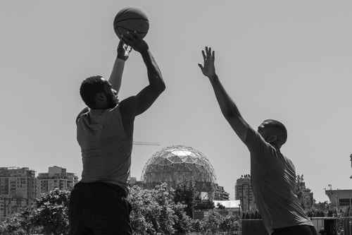 Zwei Männer spielen Basketball im Freien. Sportliche Herrenmode in Bewegung mit Fokus auf Dynamik und Freizeitstyle.