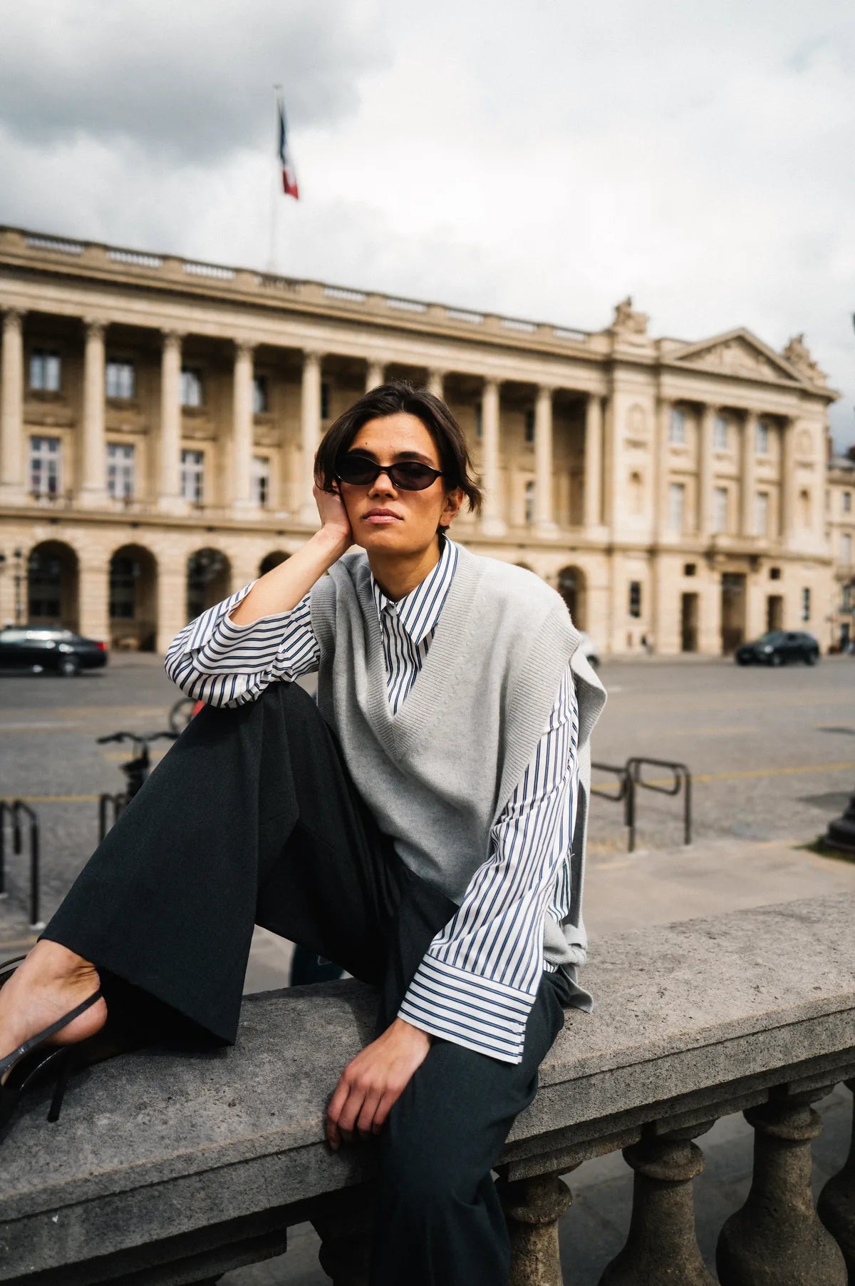 Model in grauem Pullunder und gestreifter Bluse auf einer Balustrade in Paris – Herzens Herbst/Winter 2026