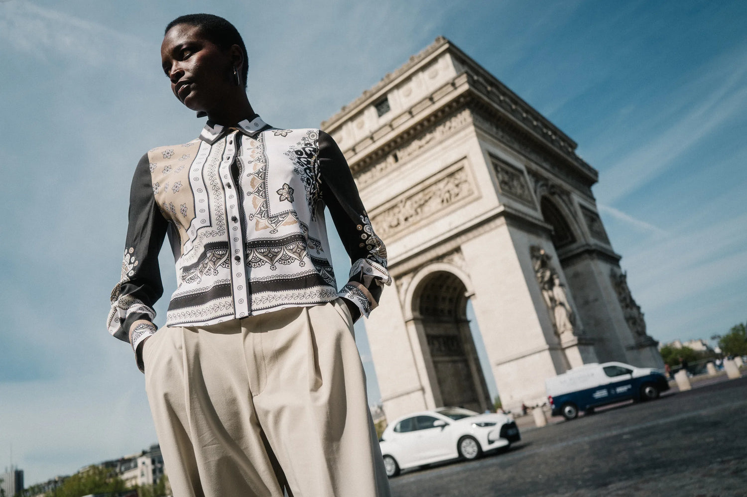 Model in gemusterter Seidenbluse und heller Bundfaltenhose vor dem Arc de Triomphe – Herzens Herbst/Winter 2026