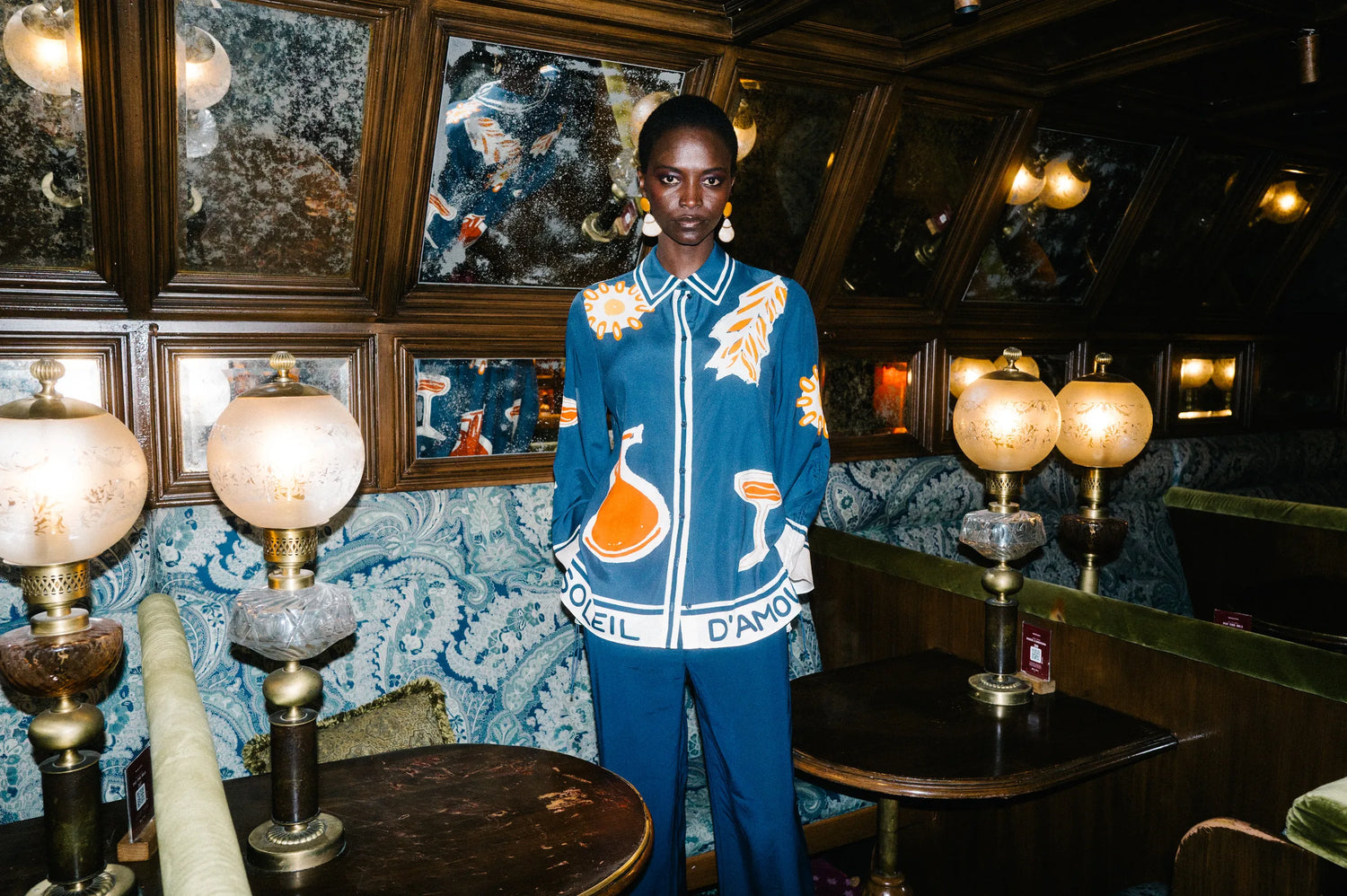 Model in blauem Seidenhemd mit Print und blauer Hose in einem Pariser Bistro – Herzens Herbst/Winter 2026